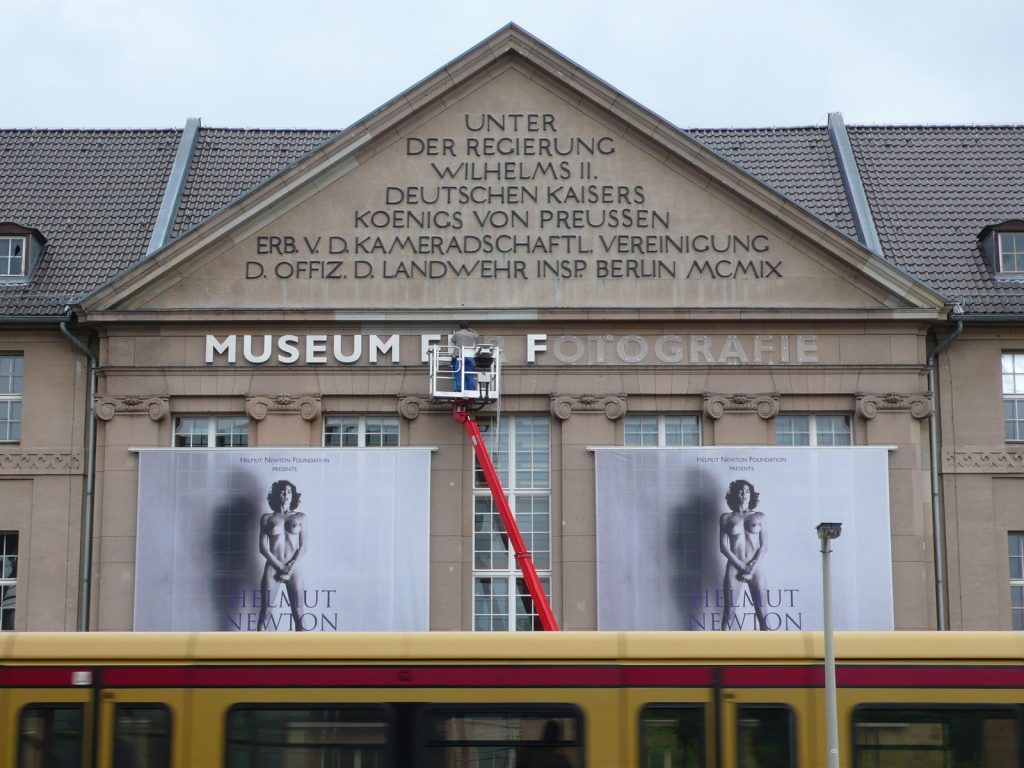 Museum für Fotografie, Berlin, Teil der Fassade, Hubbühne bei der Arbeit und große Plakate mit einem Fotomotiv von Helmut Newton, davor das Dach einer S-Bahn